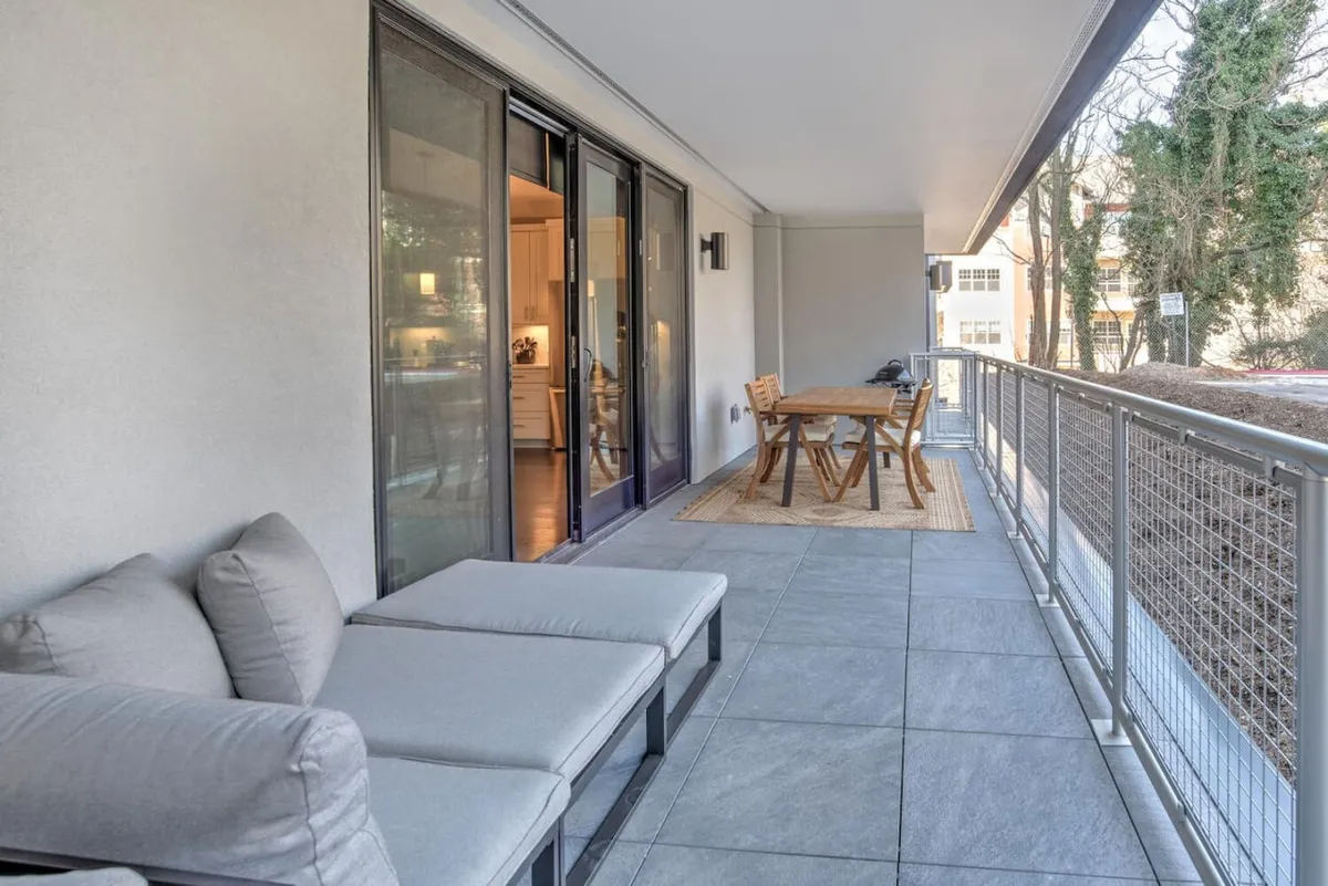 A spacious, open-air dining area on the terrace, featuring a table and chairs suitable for outdoor meals or entertaining. Sliding glass doors connect the terrace to the interior, with natural light infusing the scene. The casual atmosphere is perfect for evening gatherings or peaceful morning routines.