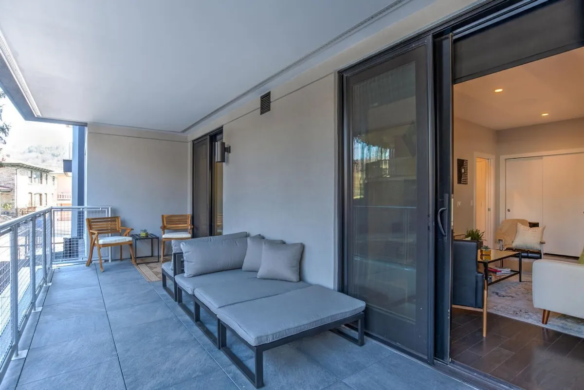 A calm, inviting outdoor seating area on a balcony or terrace, framed by a sturdy railing and featuring comfortable chairs. The setting allows clear views of the surroundings, suggesting a vantage point within the heart of downtown. The scene is captured during soft daylight, emphasizing a serene space ideal for relaxing or socializing.