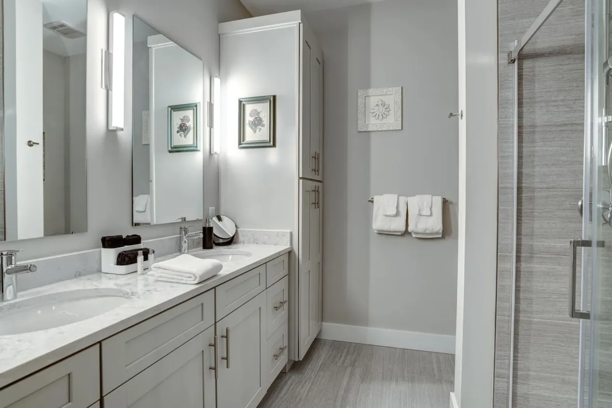 A modern bathroom featuring a double sink vanity, large mirrors, framed artwork, and a sleek shower enclosure. The space exudes a calm, spa-like ambiance, ideal for morning routines or relaxing self-care rituals.