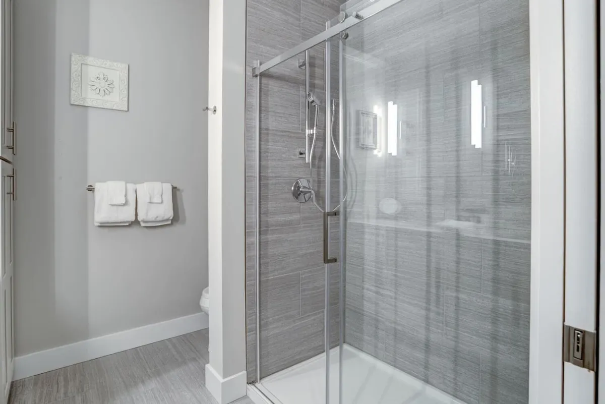 A detailed view of a contemporary bathroom with a glass shower enclosure, wall-mounted lighting, and neatly arranged towels. The design is both calming and serene, inviting refreshing showers and moments of self-care.