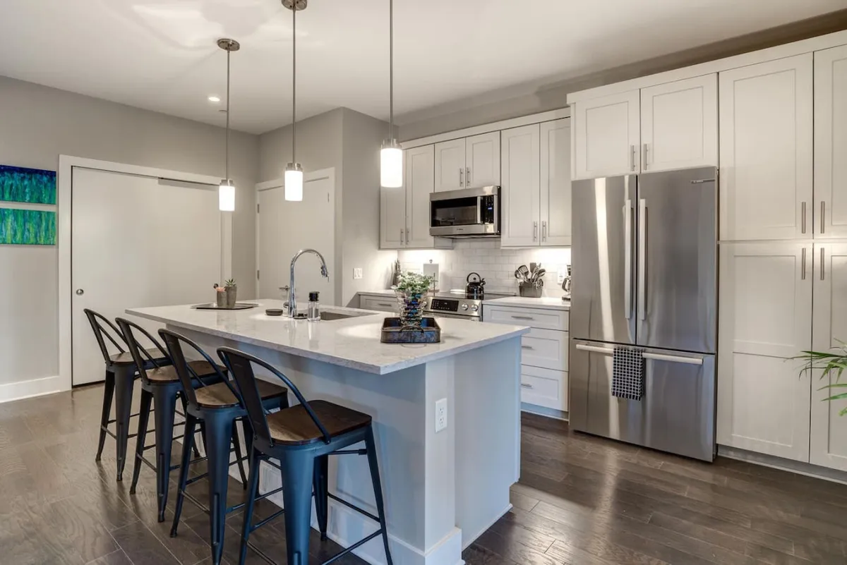 This kitchen view spotlights an island countertop, bar stools for casual dining, stainless steel appliances, and pendant lighting. The contemporary design is evident, and the scene hints at both everyday routines and special family gatherings, making it ideal for various guest needs.