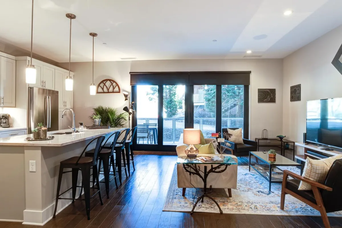 This photo presents a seamless view of the kitchen island, dining area, and living room seating with large windows illuminating the entire open-concept space. The scene suggests opportunities for gathering, sharing meals, and enjoying city views.